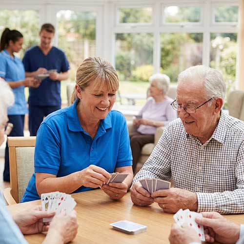 Caregiver playing cards with a resident in an assisted living common area.